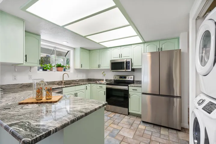 Kitchen featuring extensive cabinetry, stone-finish countertops, stainless steel appliances, and tiled flooring