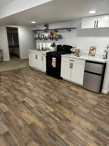 Bar area with white cabinetry, black range with gas cooktop, stainless steel refrigerator, dark wood-style flooring, and light stone counters