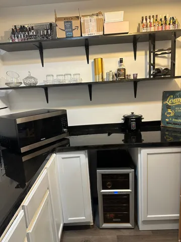 Bar with stainless steel microwave, white cabinets, beverage cooler, and dark stone countertops