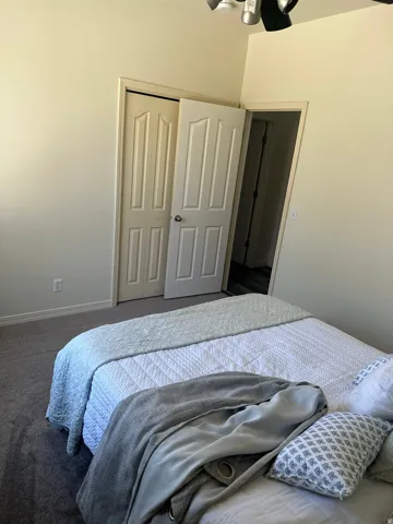 Bedroom with a closet, dark carpet, and a ceiling fan
