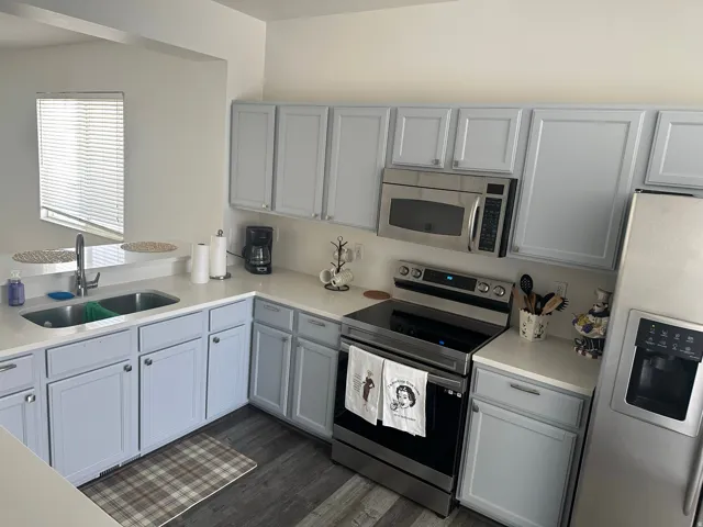 Kitchen with stainless steel appliances, light countertops, gray cabinetry, and dark wood-style flooring