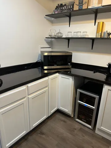 Bar with beverage cooler, stainless steel microwave, white cabinets, dark wood-style flooring, and dark stone countertops