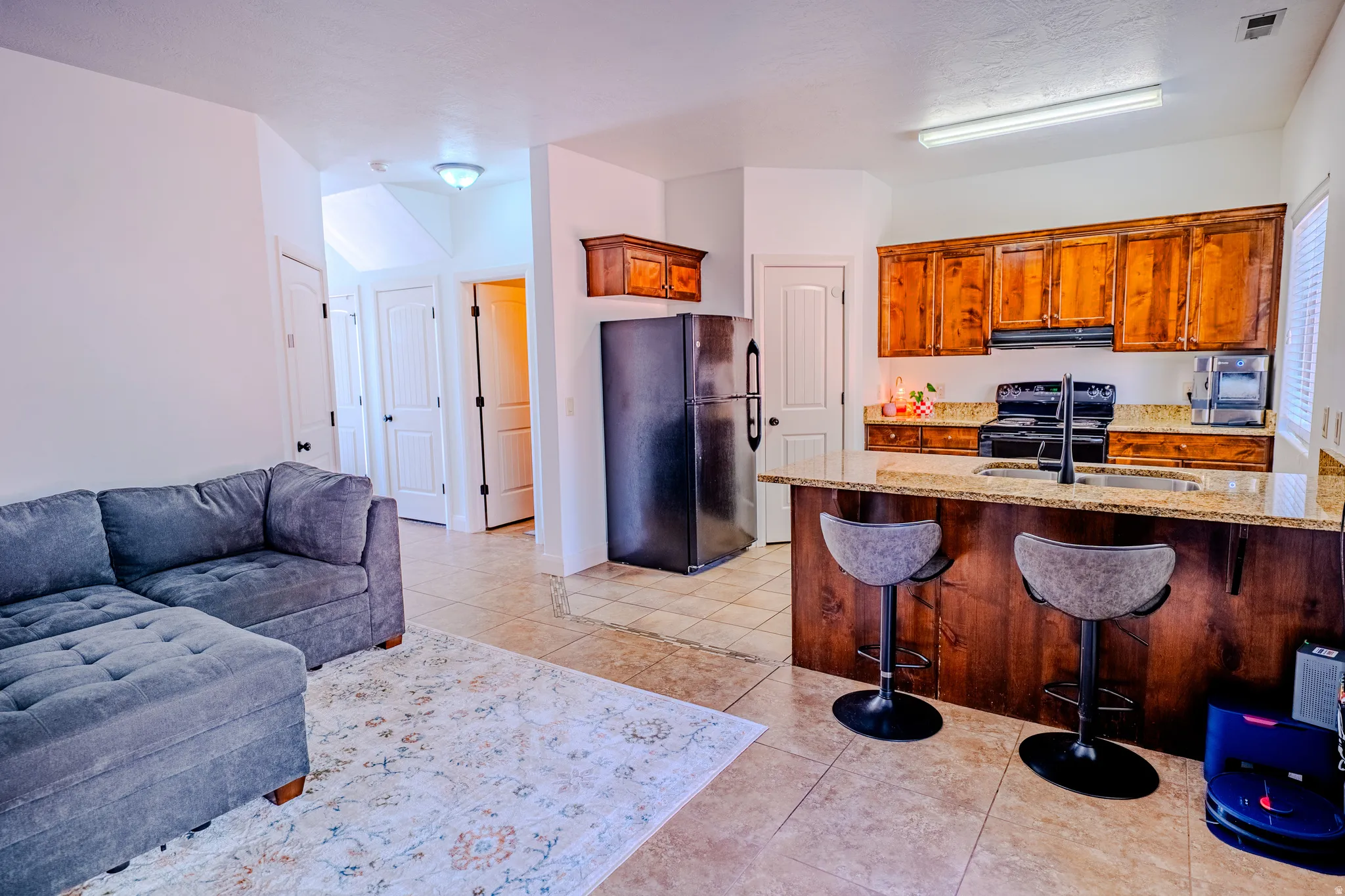Kitchen with black appliances, a breakfast bar area, light stone countertops, open floor plan, and wood finish cabinetry