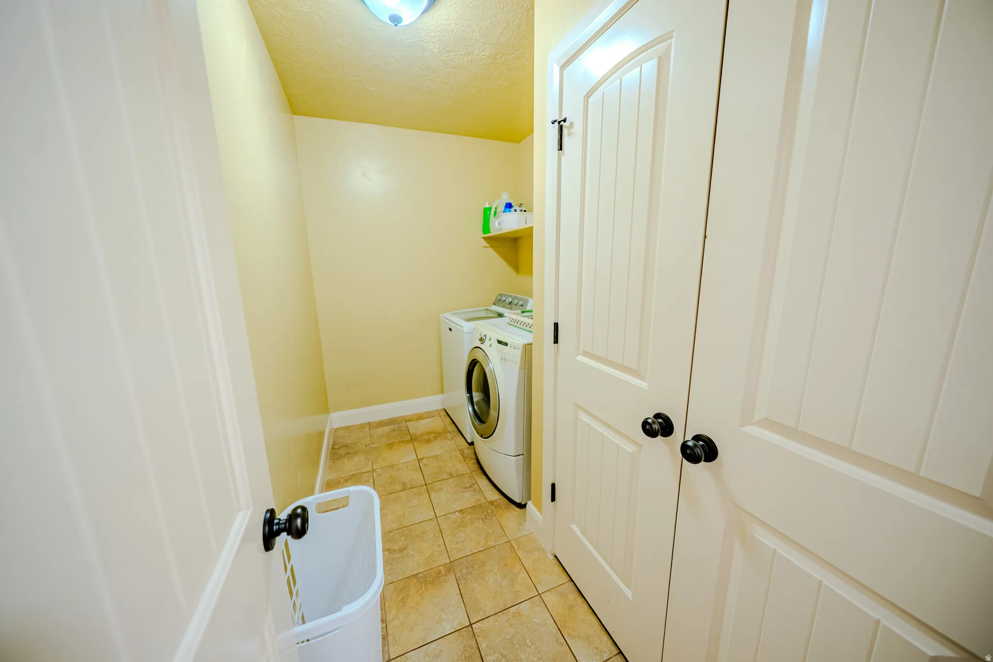 Laundry area with a textured ceiling, light tile patterned floors, and washer and clothes dryer