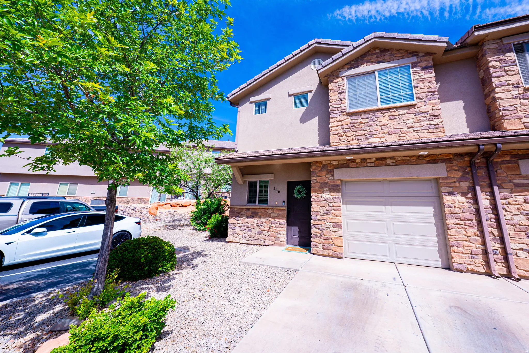 View of front of house featuring stucco siding, driveway, an attached garage, and stone siding