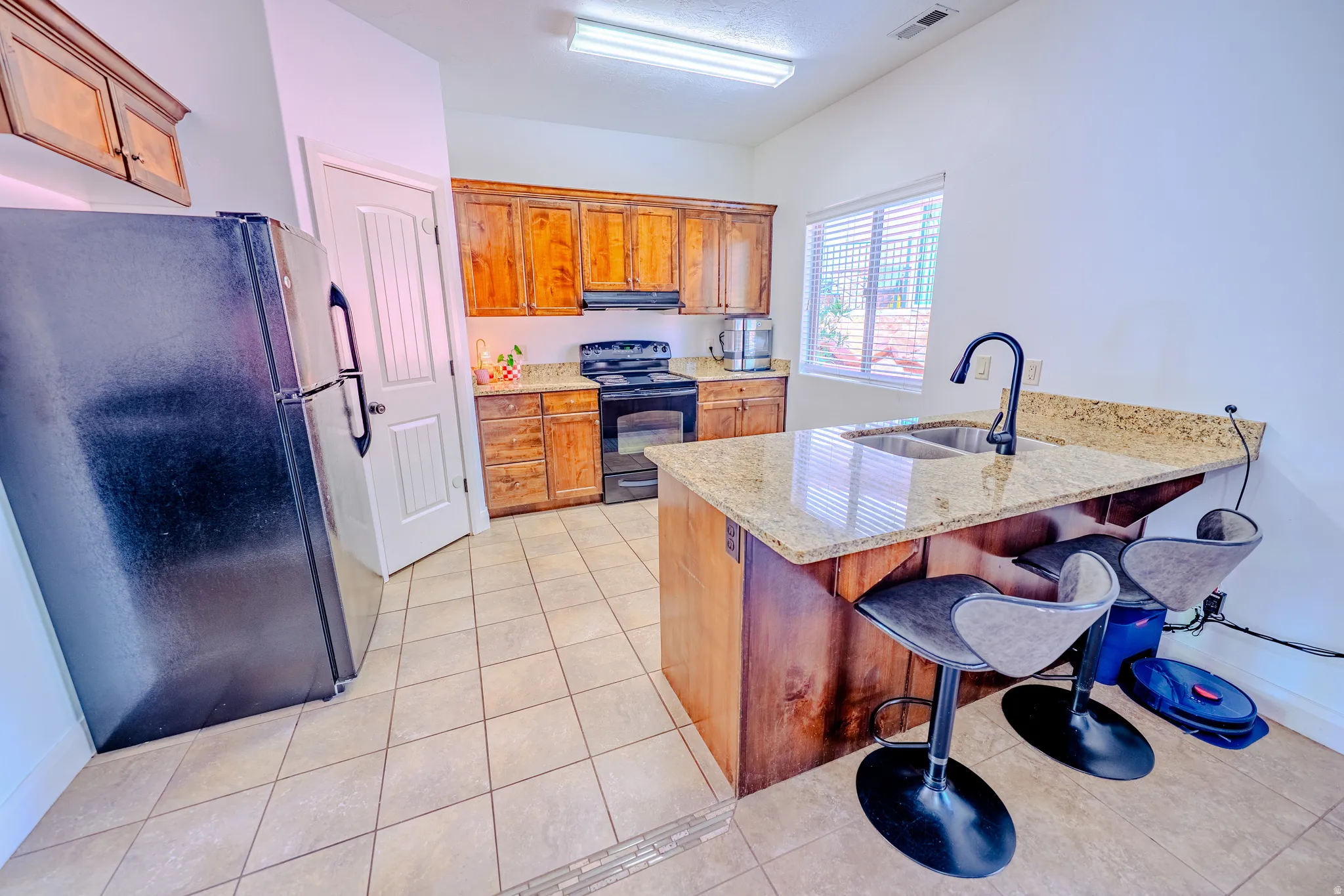 Kitchen with black appliances, a peninsula, wood finish cabinetry, a breakfast bar, and light tile patterned floors