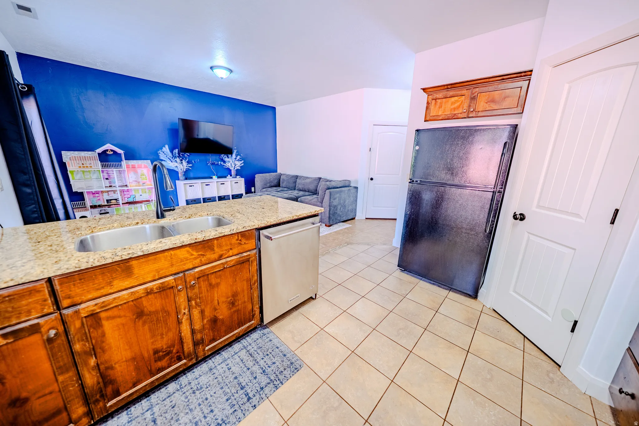 Kitchen with freestanding refrigerator, wood finish cabinets, open floor plan, light tile patterned floors, and light stone countertops