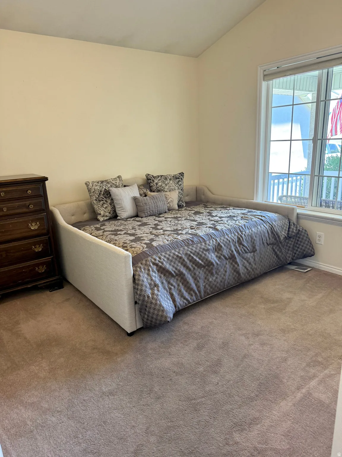 Room featuring a vaulted ceiling, large window with white framing, and neutral tone walls