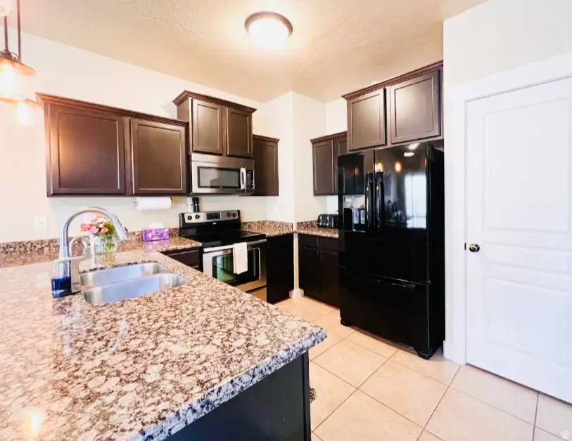 Kitchen with stainless steel appliances, dark wood finish cabinetry, light stone counters, light tile patterned floors, and a textured ceiling