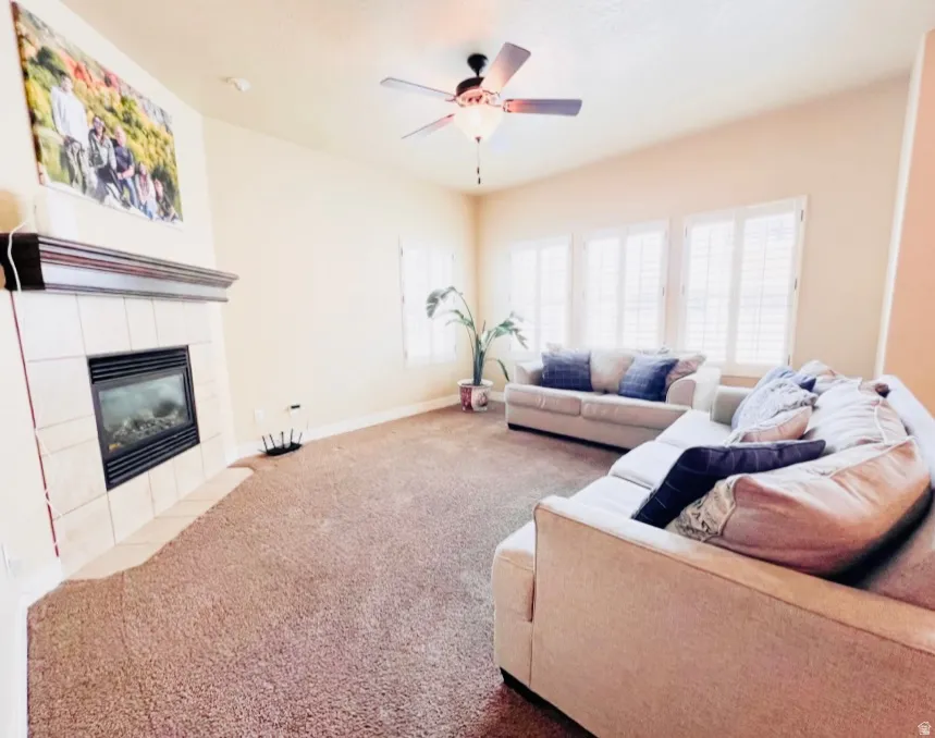 Carpeted living room with a tiled fireplace and ceiling fan