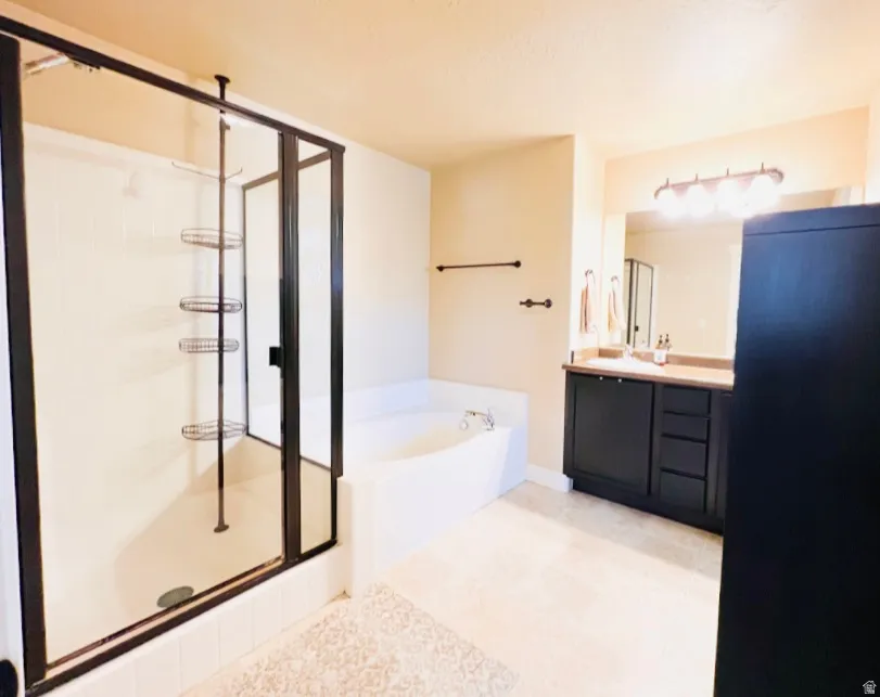 Bathroom featuring vanity, a shower stall, a garden tub, and light tile patterned flooring
