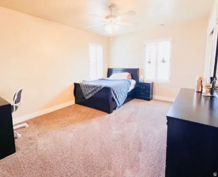 Bedroom featuring light colored carpet, a ceiling fan, and an office area