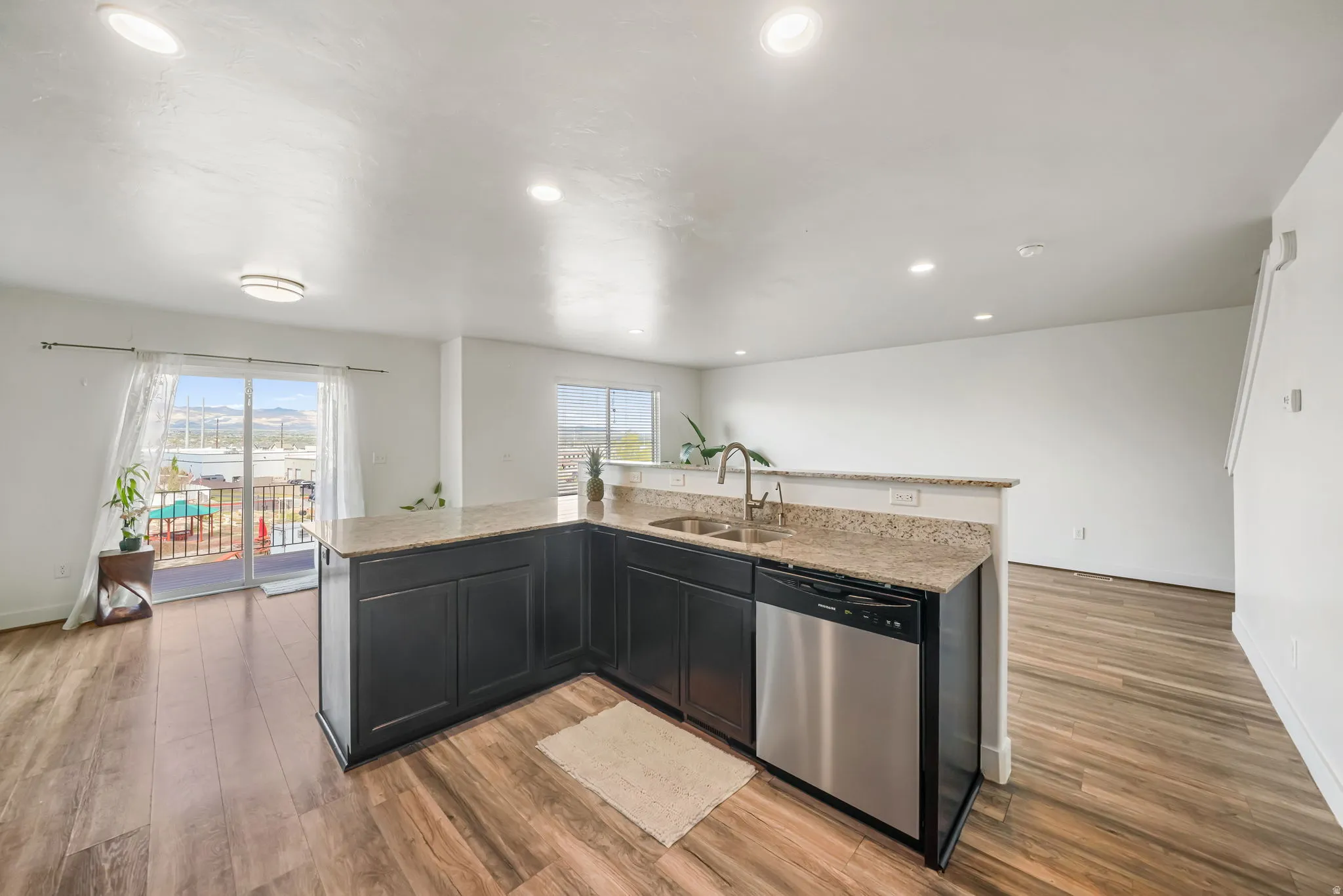 Kitchen featuring an island with sink, light stone countertops, dishwasher, dark cabinetry, and light wood finished floors