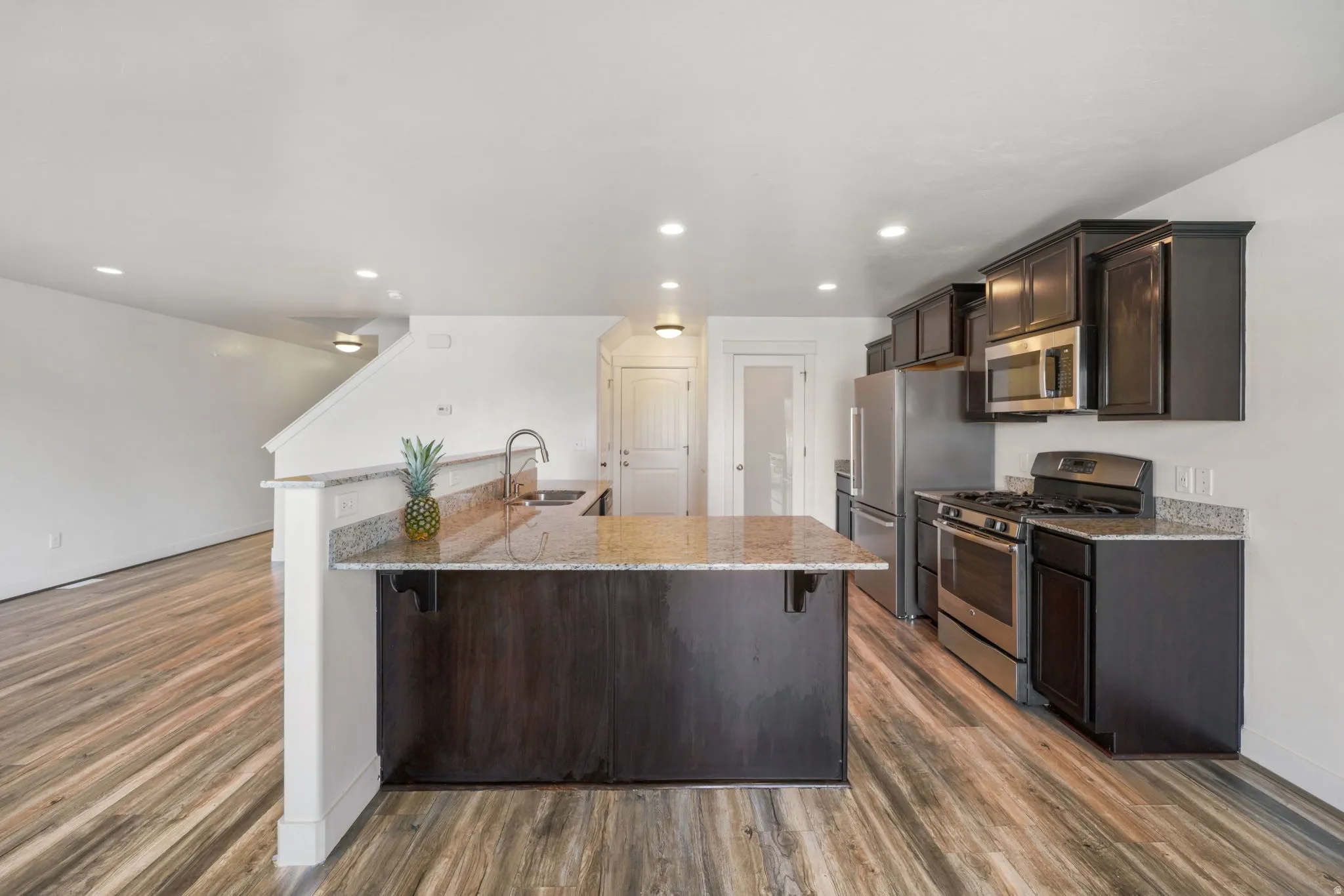 Kitchen with dark wood finish cabinets, a breakfast bar area, stainless steel appliances, light stone countertops, and dark wood-type flooring