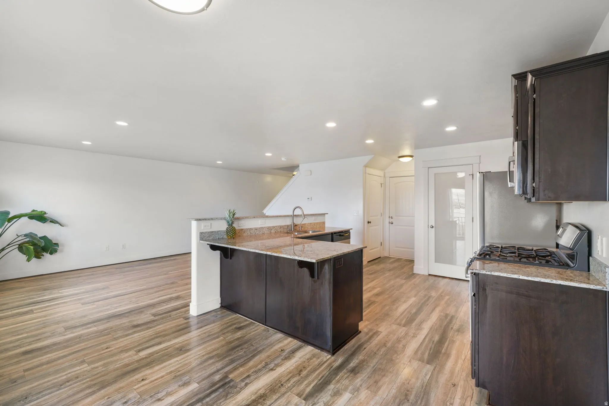 Kitchen with dark wood finish cabinetry, light stone counters, a breakfast bar area, range with gas cooktop, and light wood-type flooring