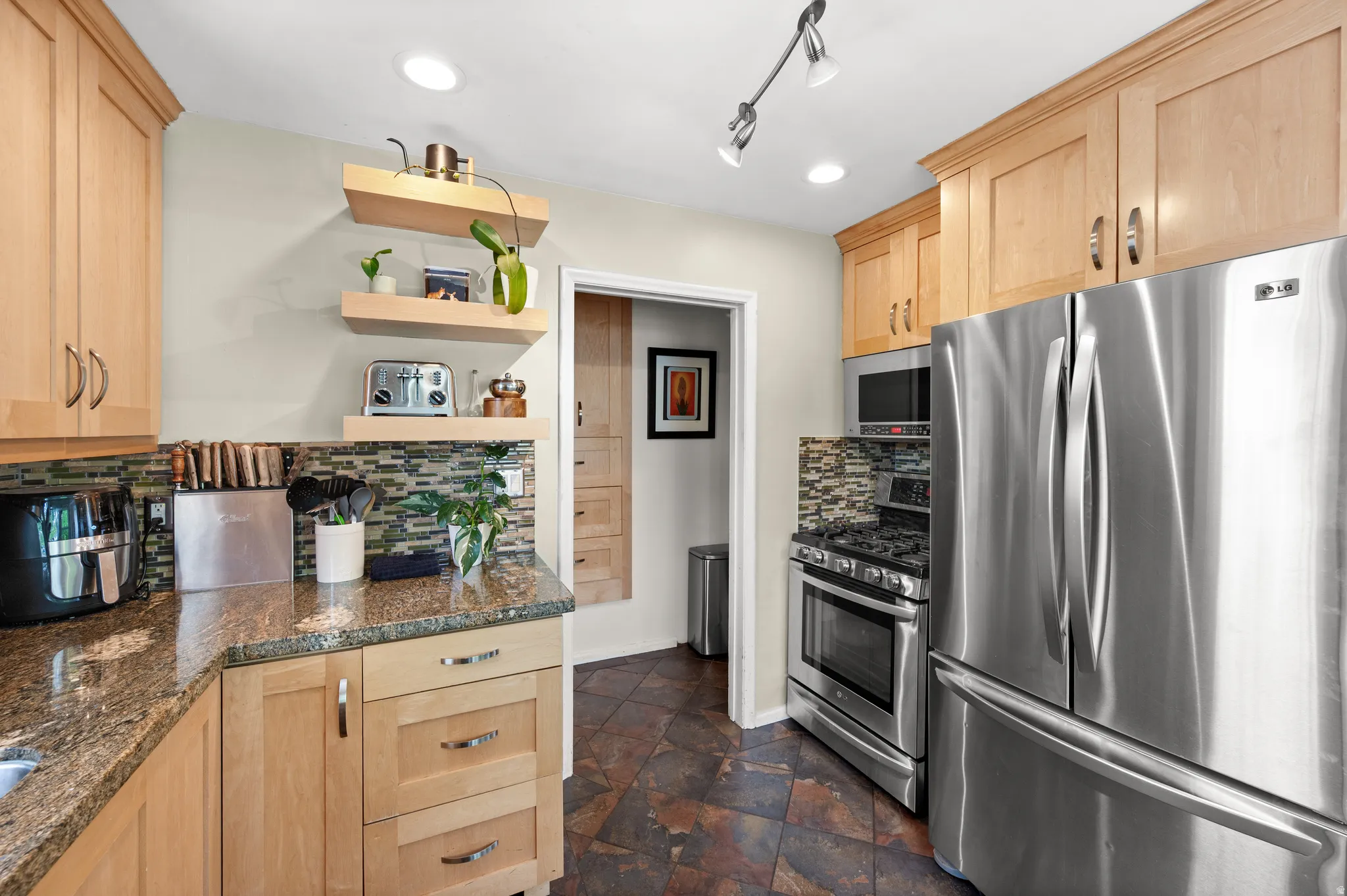 Remodeled Kitchen with light wood finish cabinets, stainless steel appliances, tasteful backsplash, and rail lighting
