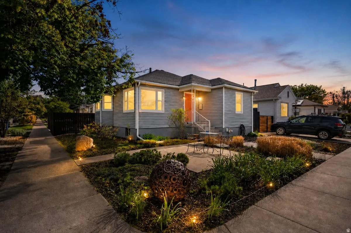 Light gray siding exterior with white trim windows and an orange front door, professional outdoor lighting