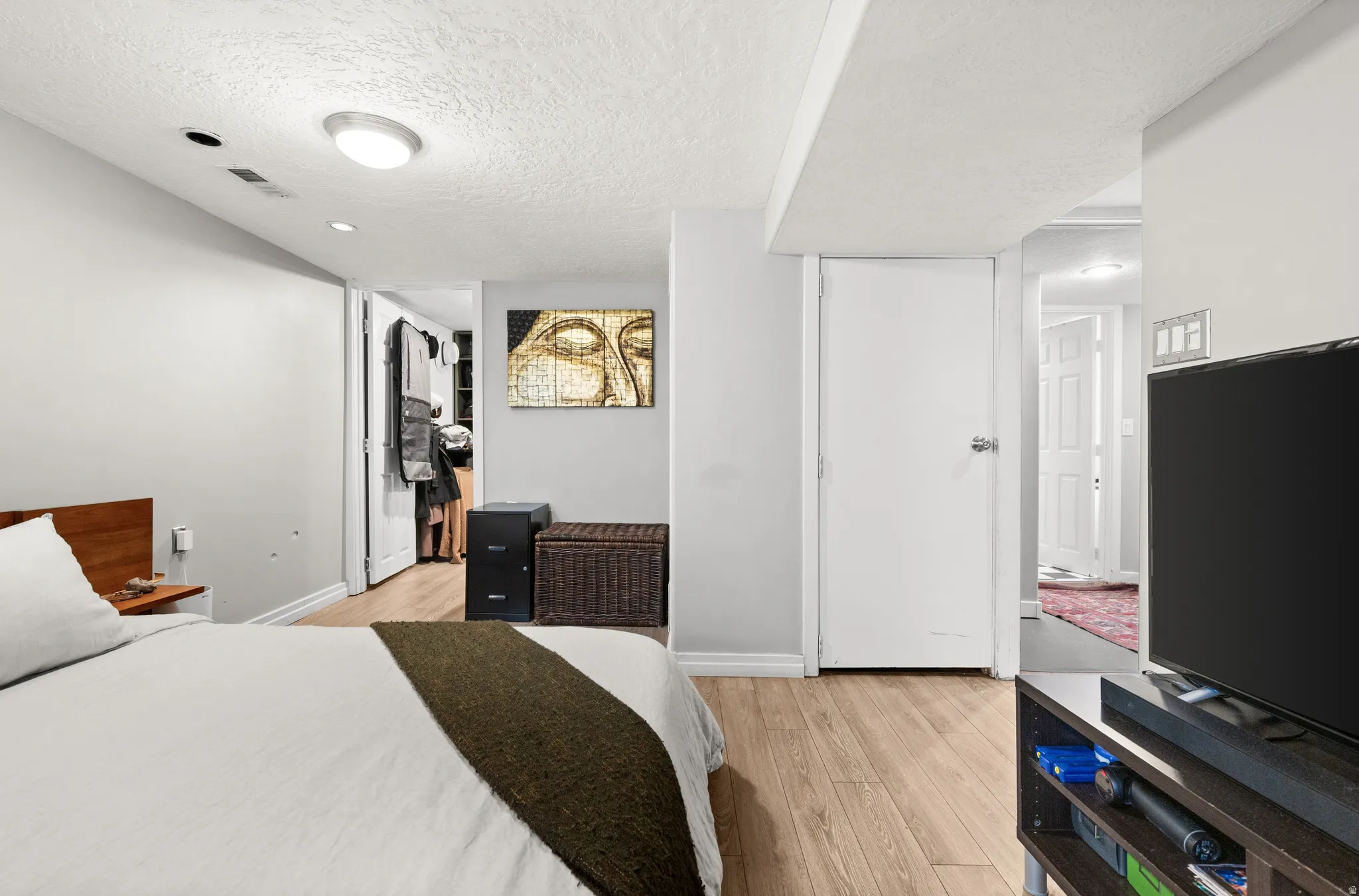 Bedroom featuring a textured ceiling, light wood-type flooring, and a walk in closet