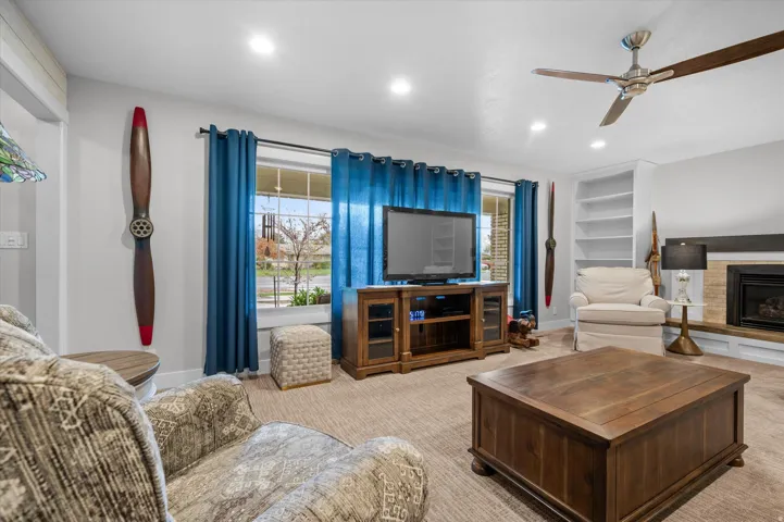 Carpeted living room featuring a glass covered fireplace, a ceiling fan, built in features, and recessed lighting