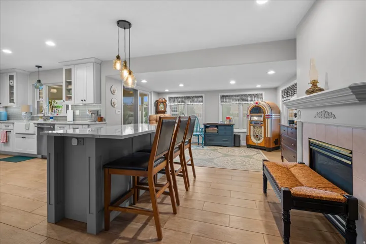 Two tone kitchen featuring two tone cabinets, glass fronted cabinets, a tiled fireplace, a center island, and a breakfast bar