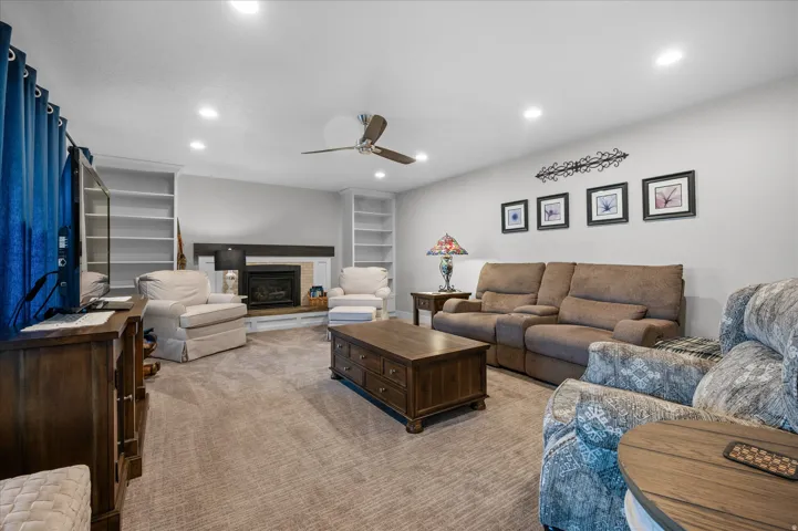 Carpeted living room with a ceiling fan, recessed lighting, a glass covered fireplace, and built in features
