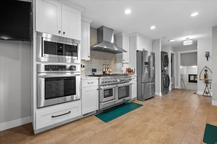 Kitchen with high quality appliances, custom white cabinetry, recessed lighting, decorative backsplash, and stacked washing machine and dryer
