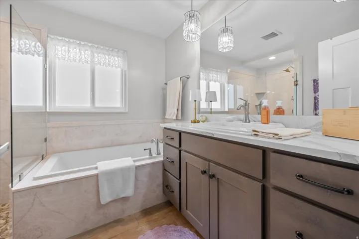 Full bathroom with vanity, a garden tub, a stall shower, suspended lighting, and light wood finished floors