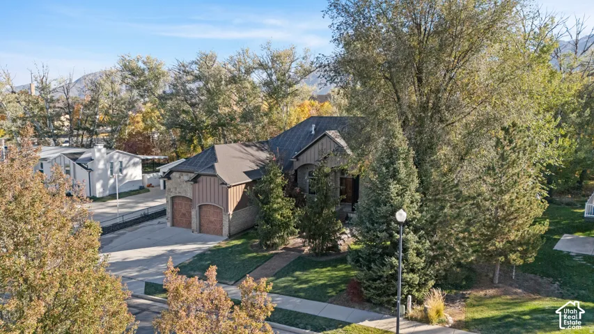 View of front of property with stone siding, concrete driveway, board and batten siding, a garage, and view of wooded area