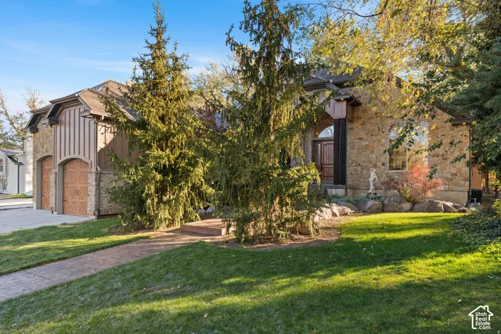 Obstructed view of property featuring a front lawn, board and batten siding, stone siding, and driveway