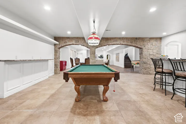 Recreation room featuring a classic pool table, stone archways, and a built-in bar with stone-finish countertops