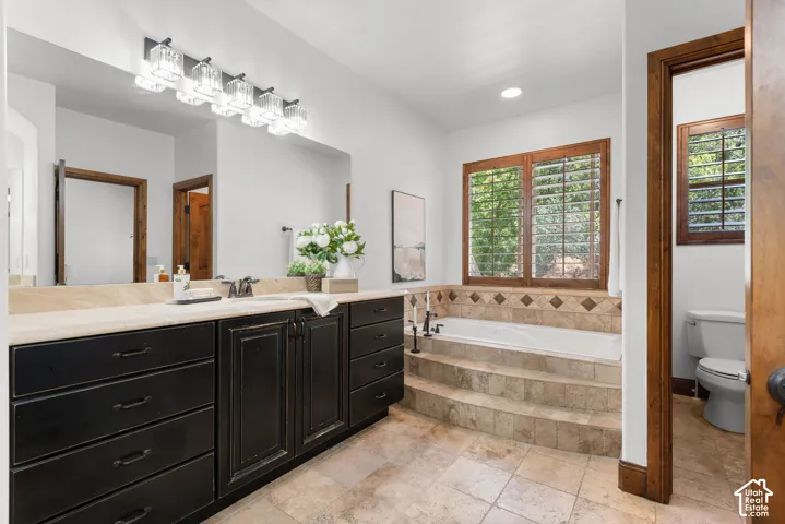 Spacious bathroom featuring a dual vanity with dark cabinetry, light-toned countertop, and an integrated soaking tub with tiled surround and steps