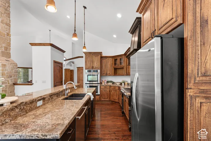 Kitchen featuring rich wood cabinetry, stainless steel appliances, a large island with a dual-basin sink, and stone countertops