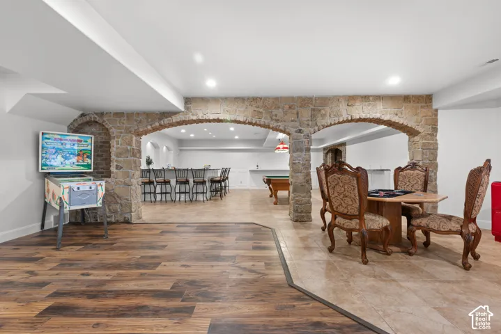 Expansive recreational area featuring wood-finish flooring, stone archways, recessed lighting, and a tiled section