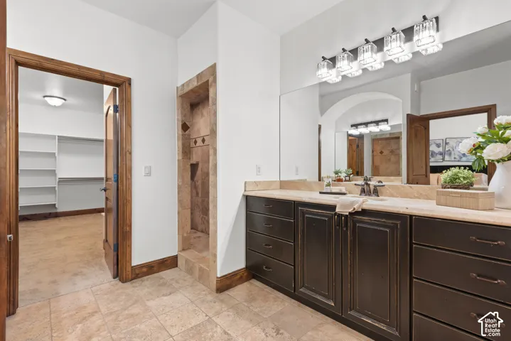 Tiled bathroom flooring featuring a spacious vanity with dual sinks, an expansive mirror, and a five-light fixture
