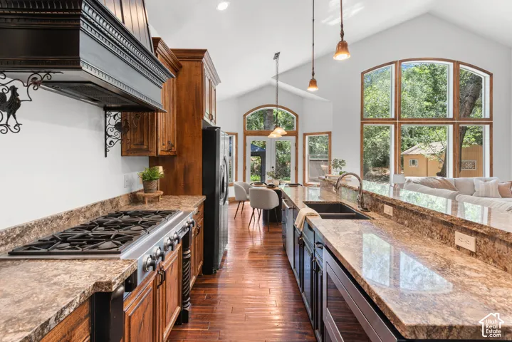 Gourmet kitchen with gas range, stone-finish countertops, wood cabinetry, and a large kitchen island with integrated sink