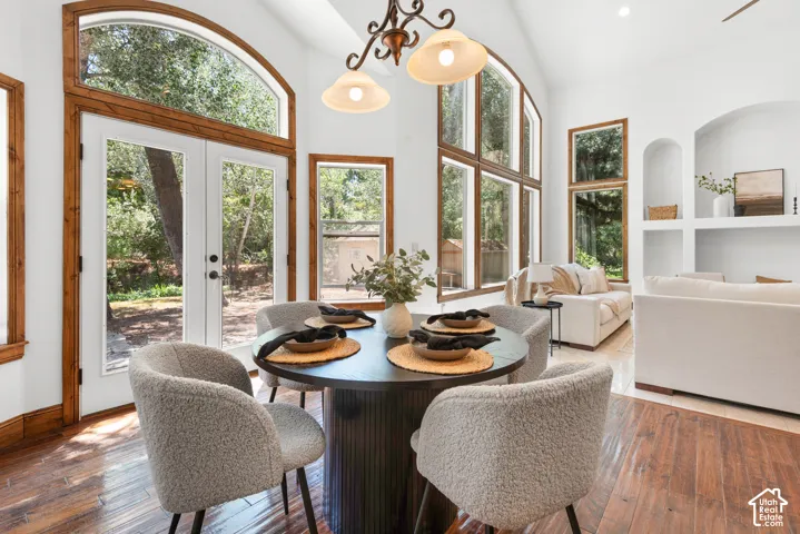 Vaulted ceiling dining area featuring hardwood flooring, an arched glass-paned double door, and multiple large windows with natural wood trim