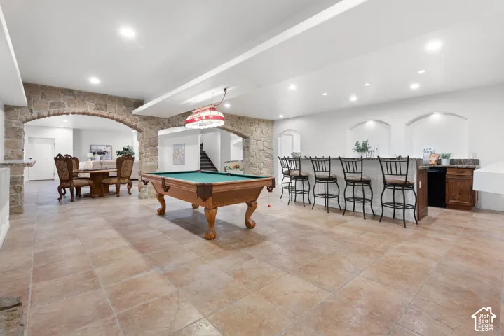 Spacious recreation area featuring stone archways, recessed lighting, tile flooring, a built-in bar with countertop, and display niches