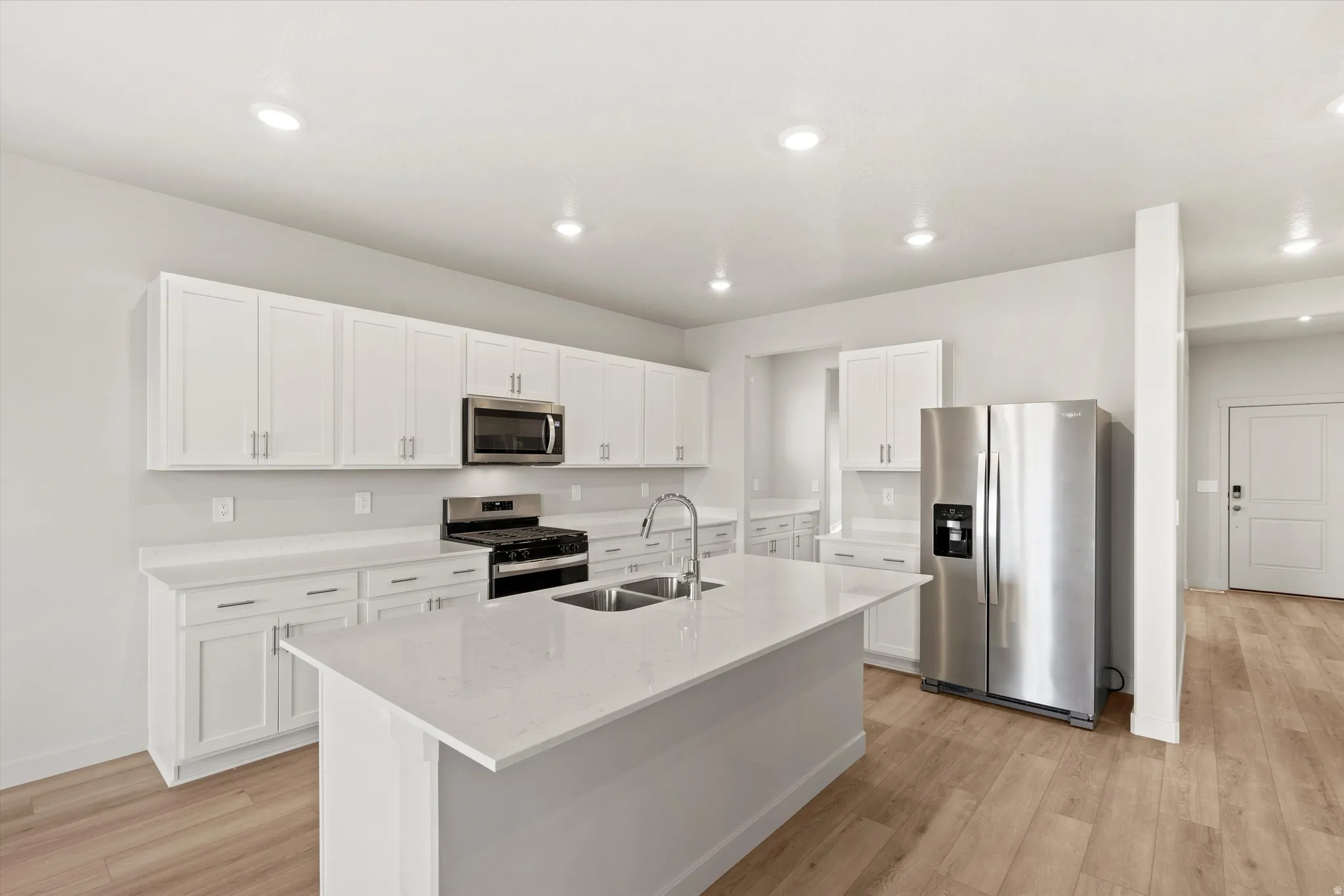 Kitchen featuring stainless steel appliances, white cabinets, light wood-style floors, light stone countertops, and an island with sink