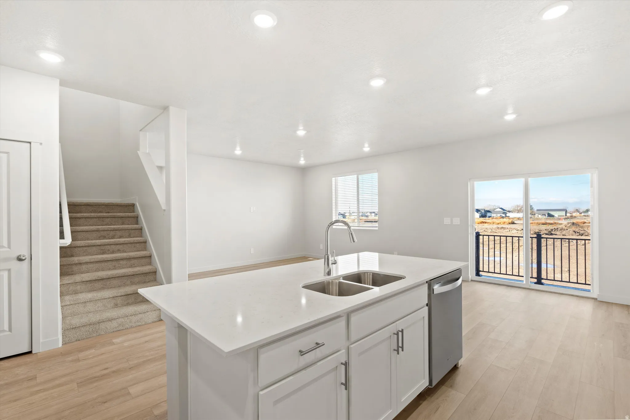 Kitchen with light wood finished floors, light stone countertops, white cabinetry, an island with sink, and recessed lighting