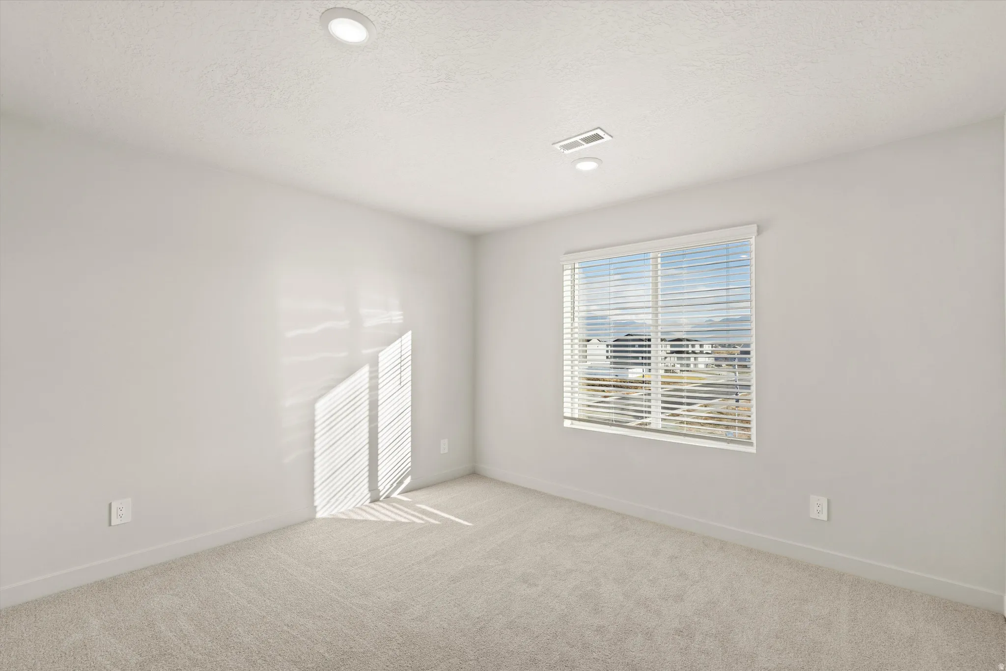 Empty room with light colored carpet, a textured ceiling, and recessed lighting