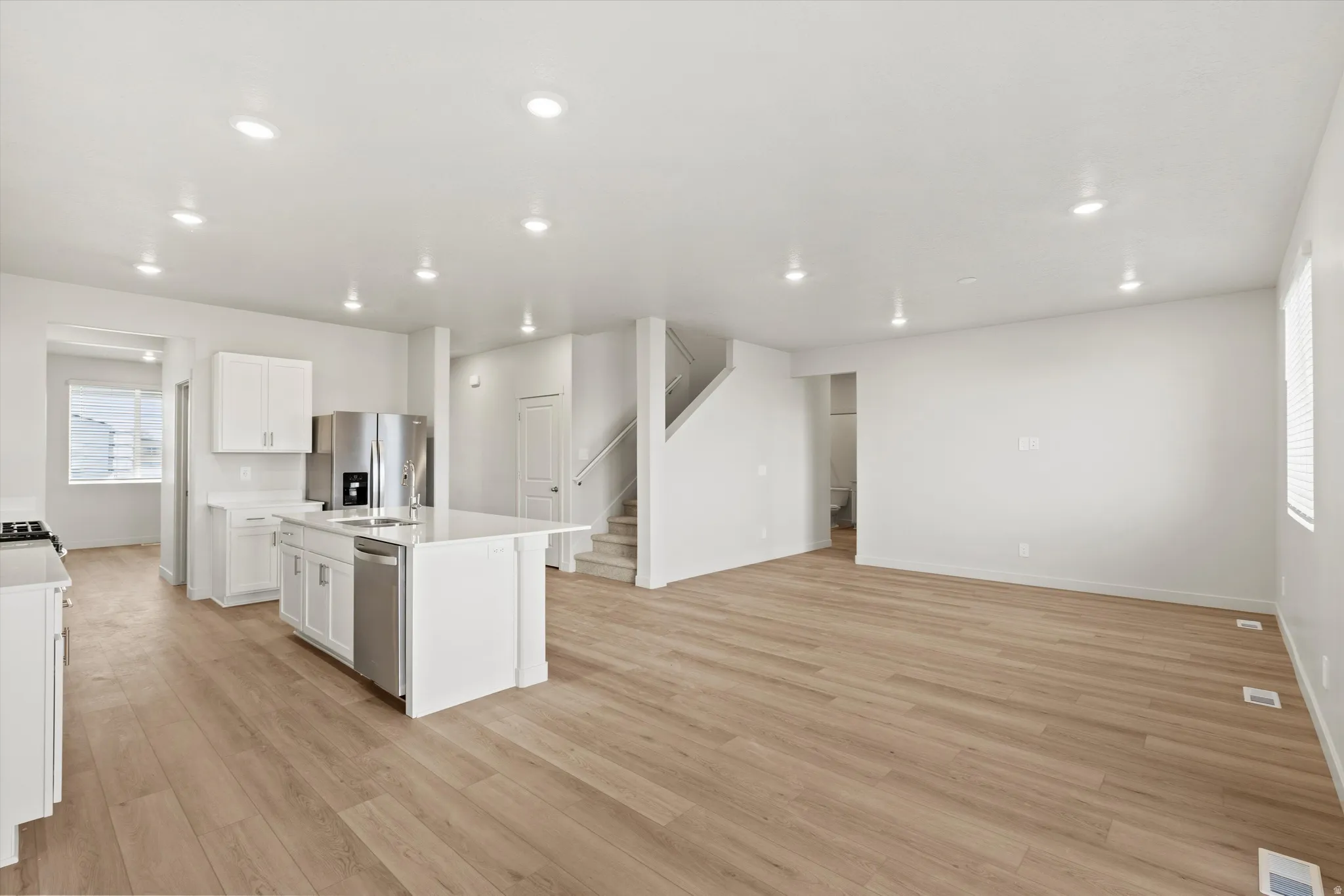 Kitchen featuring an island with sink, stainless steel appliances, light wood-type flooring, white cabinets, and open floor plan