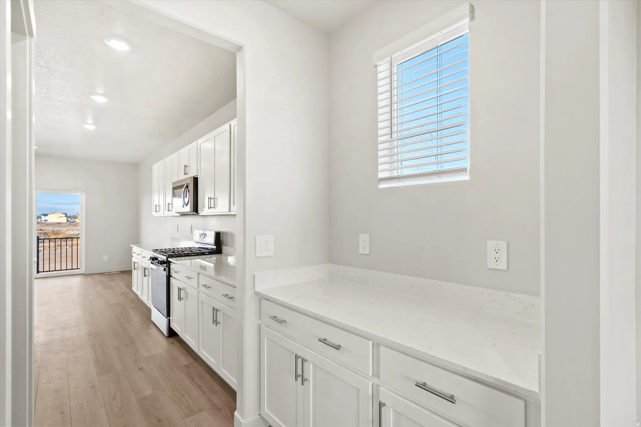 Kitchen featuring stainless steel appliances, white cabinetry, light wood-style floors, light stone counters, and recessed lighting