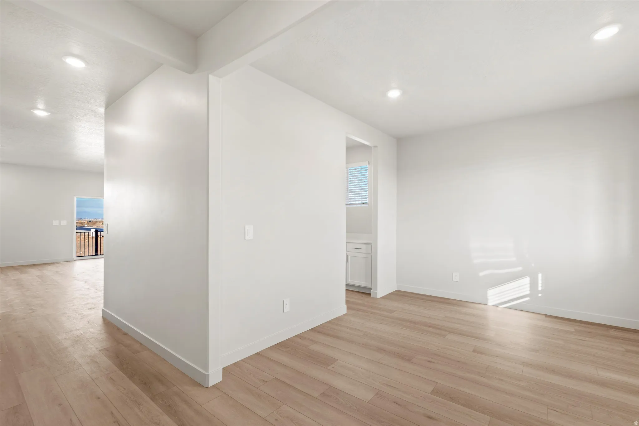 Empty room with recessed lighting, beam ceiling, and light wood-style floors