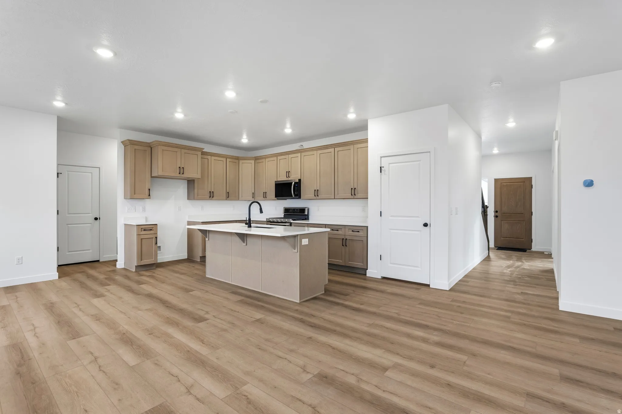 Kitchen with a kitchen bar, an island with sink, stainless steel appliances, light wood-style flooring, and recessed lighting