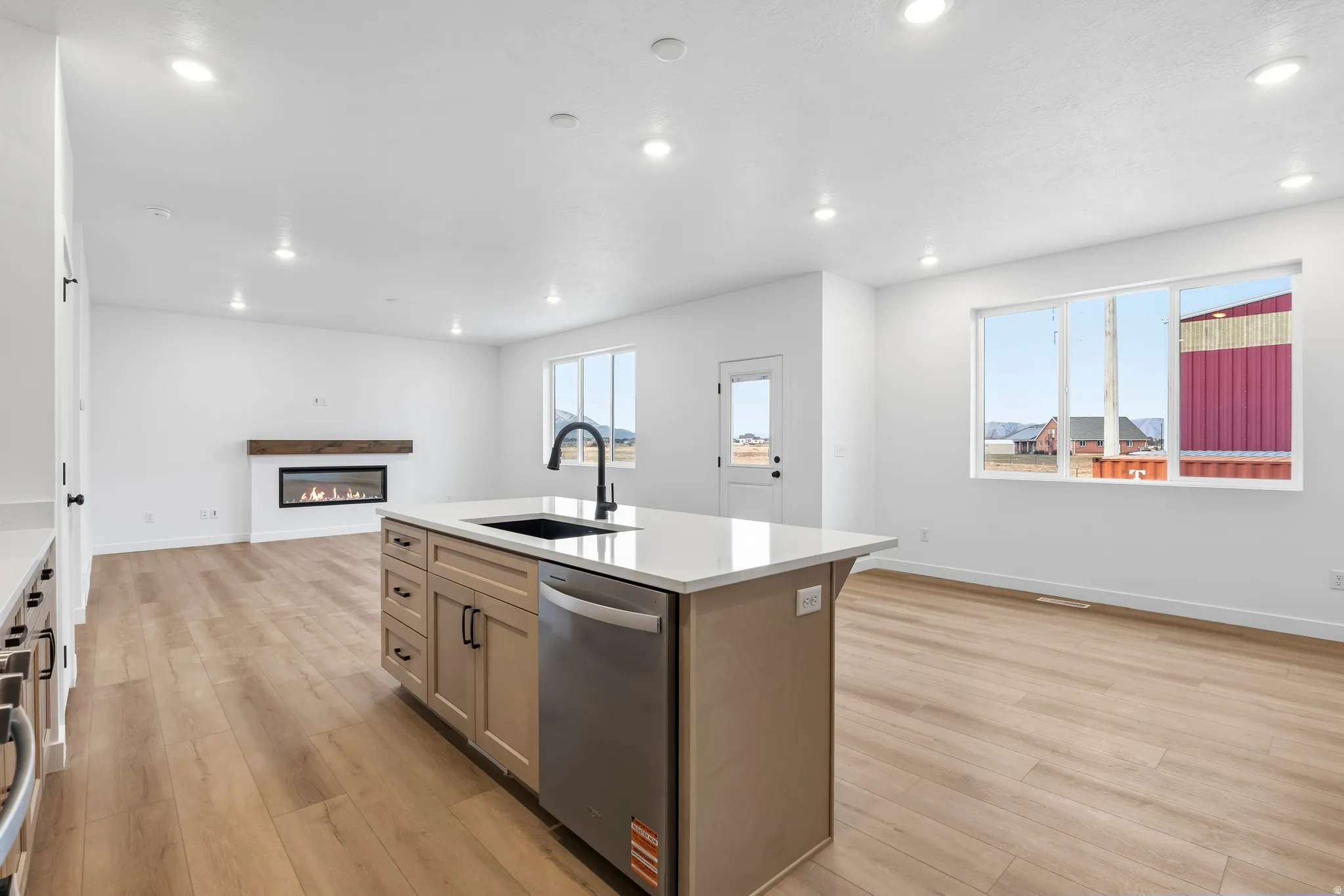 Kitchen featuring open floor plan, a glass covered fireplace, a center island with sink, light wood finished floors, and light stone countertops