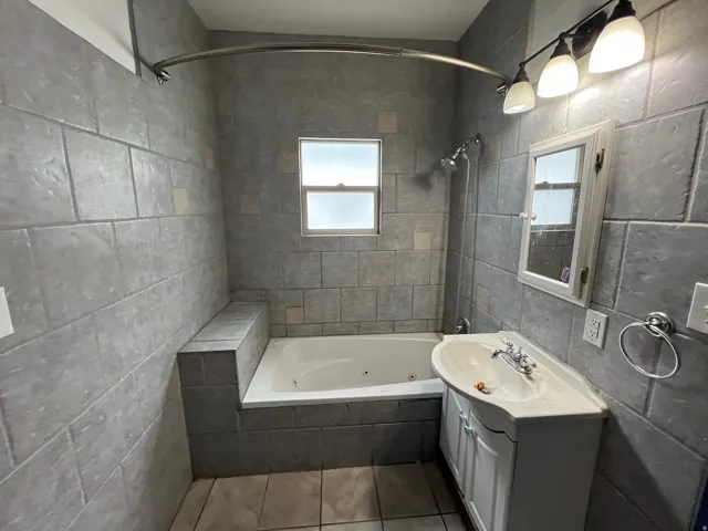 Full bathroom with tile walls, vanity, a combined bath / shower with jetted tub, and dark tile patterned flooring