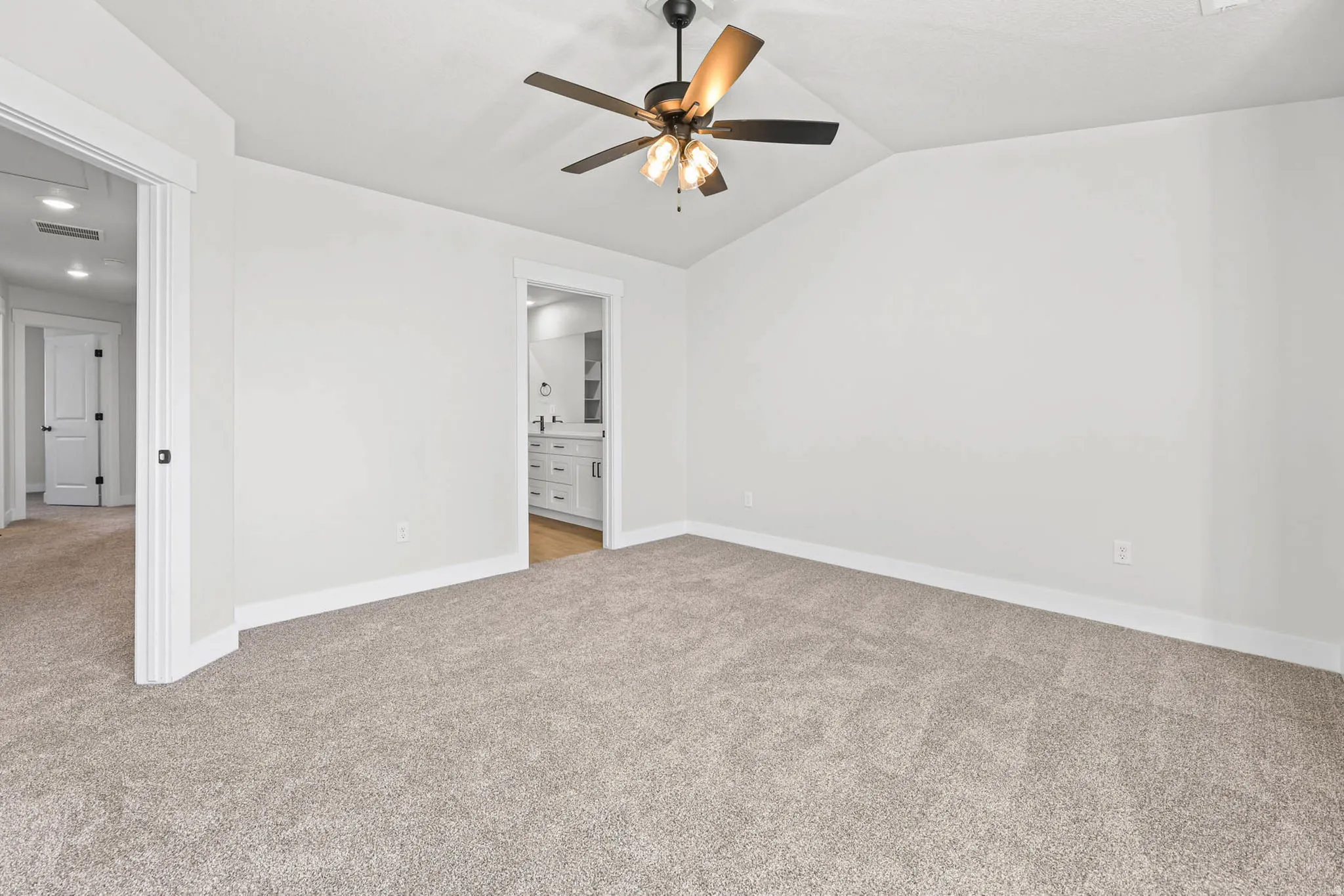 Unfurnished bedroom featuring light carpet, ensuite bathroom, a ceiling fan, and vaulted ceiling