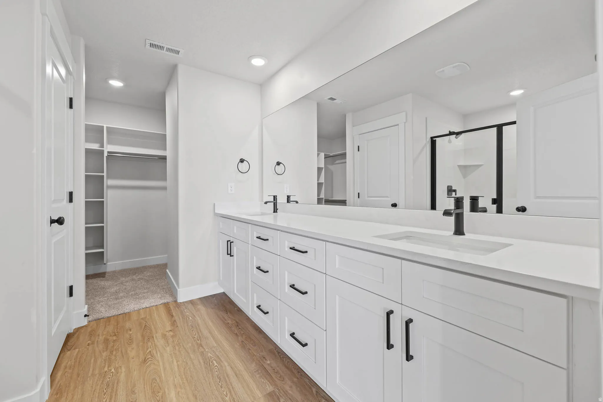 Bathroom featuring a stall shower, a walk in closet, double vanity, light wood-type flooring, and recessed lighting
