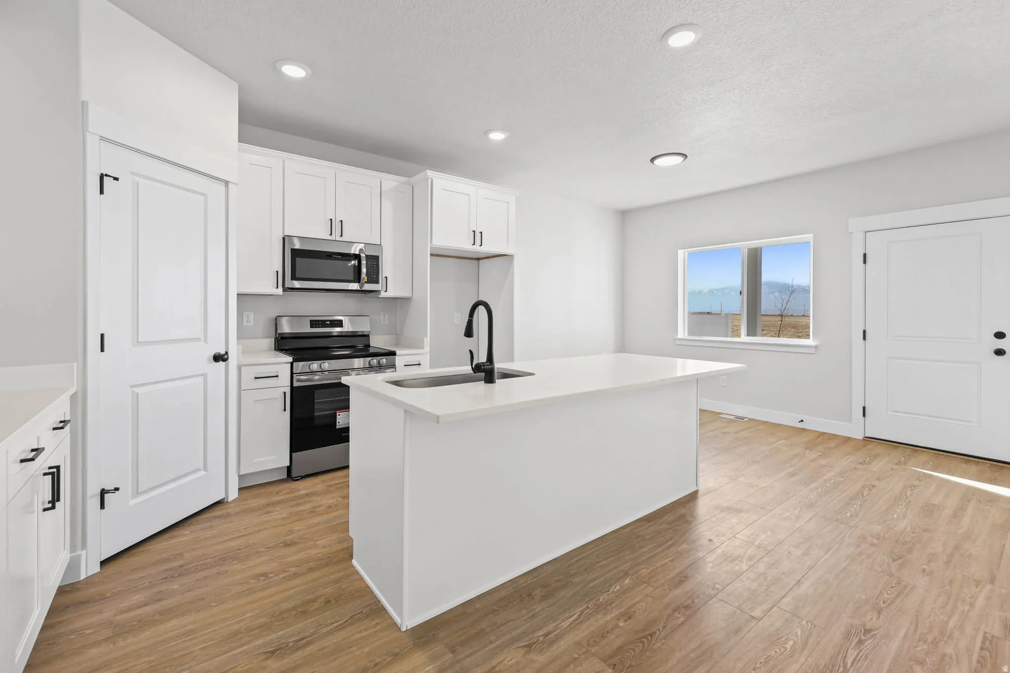 Kitchen featuring an island with sink, stainless steel appliances, light wood finished floors, white cabinetry, and a textured ceiling