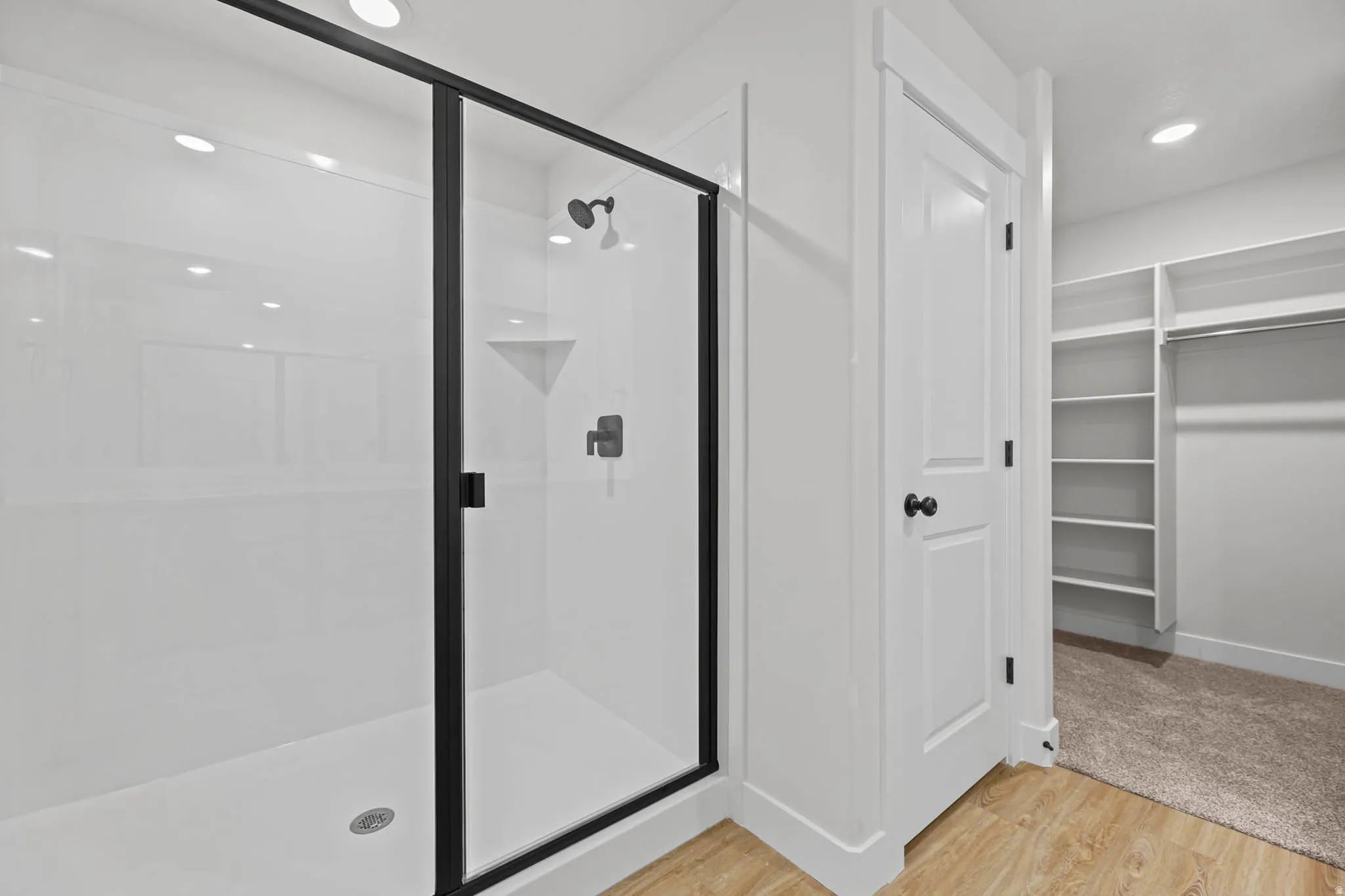 Bathroom featuring a walk in closet, a stall shower, light wood-style floors, and recessed lighting
